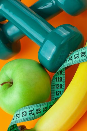 dumbells with measuring tape and fruits on color backgroundの写真素材