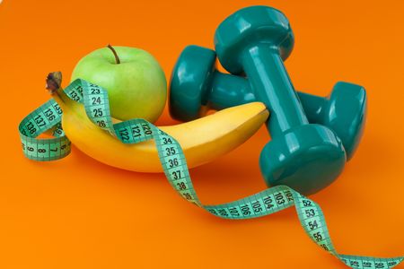 dumbells with measuring tape and fruits on color backgroundの写真素材