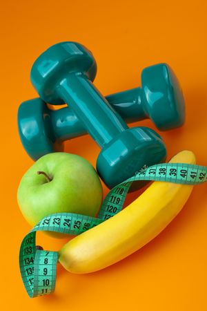 dumbells with measuring tape and fruits on color backgroundの写真素材