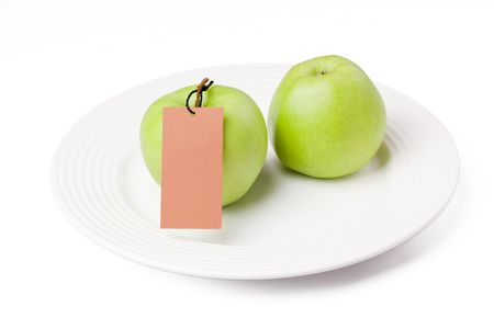 the photo shot of green apples with label on white plateの写真素材