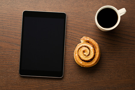 Cinnamon roll, cup of coffee and computer tablet. Business breakfast.