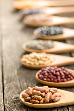 various dried legumes in wooden spoons on old tableの写真素材