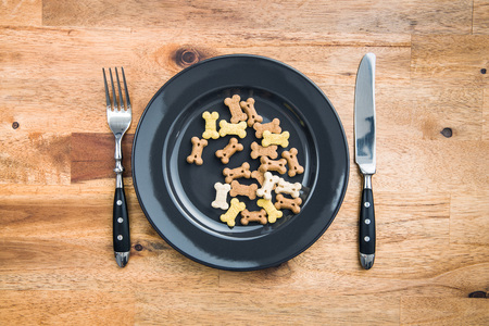 Dog food shaped like bones on plate and cuttlery. Top view.の写真素材