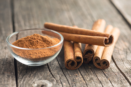 Cinnamon sticks and ground cinnamon on old wooden table.