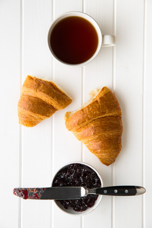 Tasty buttery croissant, cup of black tea and jam in jar. Top view.の写真素材