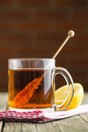 Tea cup with sugar crystal on wooden stick on old wooden table.の写真素材