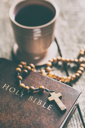 Rosary beads, holy bible and cup of wine on wooden table.の写真素材