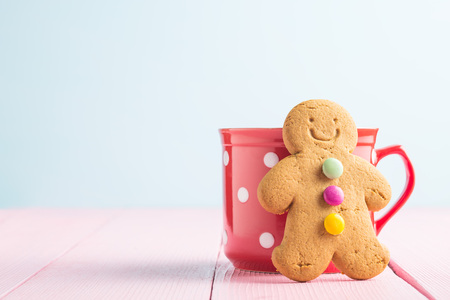Gingerbread man leaning against a cup on pink table. Xmas gingerbread.の写真素材