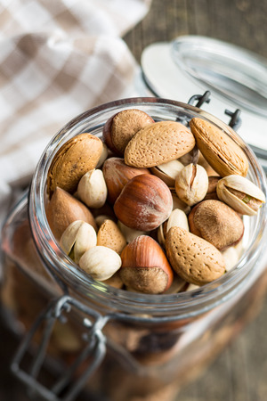 Different types of nuts in the nutshell. Hazelnuts, walnuts, almonds, pecan nuts and pistachio nuts in jar.の写真素材