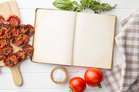 Old recipe book with tomatoes, dried tomatoes, herbs and salt. Top view on cookbook.の写真素材