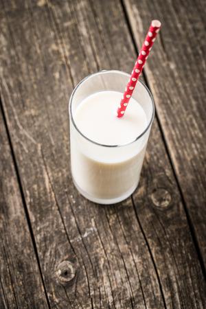 Glass of milk and red straw on old wooden table.の写真素材