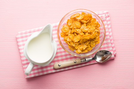 Breakfast cereals or cornflakes and milk on checkered napkin. Top view.