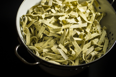 Raw italian pasta. Dry noodles with spinach in colander.の写真素材