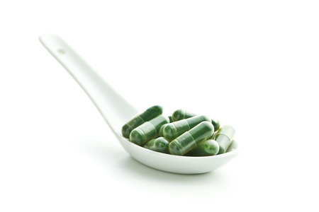 Green chlorella pills or green barley pills in spoon isolated on white background.の写真素材