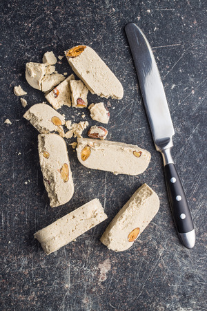 Sweet halva dessert slices with almonds and knife on old kitchen table. Top view.の写真素材