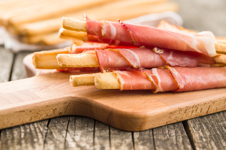 Parma ham prosciutto with grissini breadsticks on cutting board.の写真素材