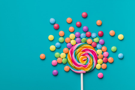 Sweet lollipop and colorful chocolate candy pills on blue background.