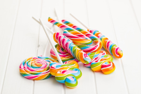 Various colorful lollipops on white wooden table.