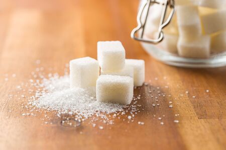Sweet white sugar cubes on wooden table.
