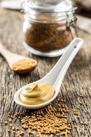 Yellow mustard in ceramic spoon and mustard seeds on old wooden table.の写真素材
