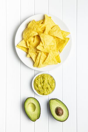 Corn nacho chips and avocado dip. Yellow tortilla chips and guacamole on white table. Top view.の写真素材