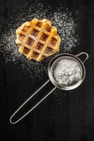 Belgian waffles sprinkled with sugar on black table. Top view.の写真素材