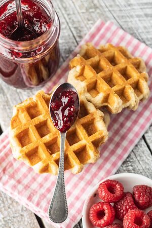Tasty sweet waffles with raspberries and jam on white wooden table.の写真素材