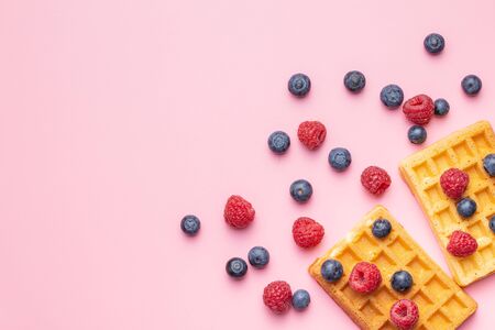 Waffles with blueberries and raspberries on pink background. Top view.