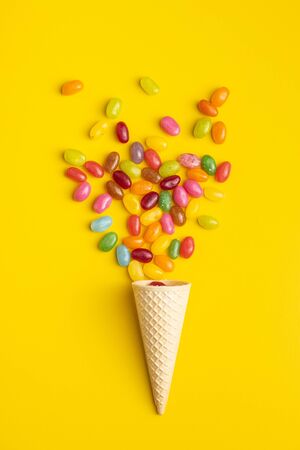 Fruity jellybeans. Tasty colorful jelly beans and waffle cone on yellow background. Top view.の写真素材
