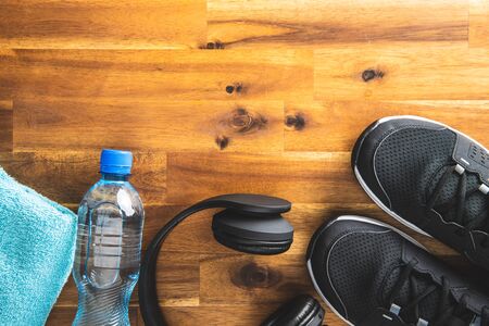 Fitness concept. Black sports shoes, headphones, dumbbell and bottle of water on wooden floor. Top view.の写真素材