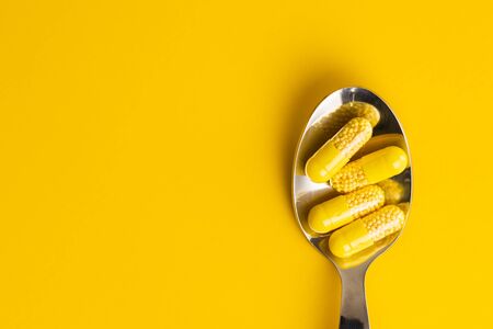 Vitamin capsules. Vitamin C pills in spoon on yellow background. Top view.の写真素材