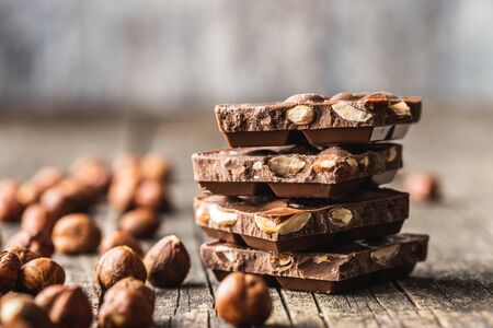 Dark nut chocolate and hazelnuts. Broken chocolate bar on black kitchen table. Pile of chocolate on...
