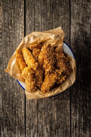 Breaded fried chicken strips in bowl on old wooden table. Tasty fast food.Top view.の写真素材