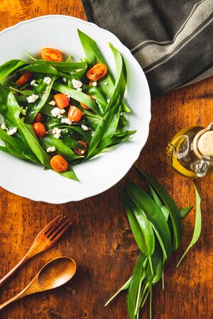 Fresh salad with wild garlic,tomatoes and feta cheese on plate. Ramsons leaves. Top view.の写真素材