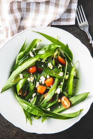 Fresh salad with wild garlic,tomatoes and feta cheese on plate. Ramsons leaves. Top view.