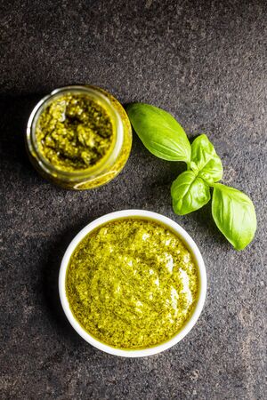 Green basil pesto dip sauce in bowl and basil leaves on black table. Top view.の写真素材