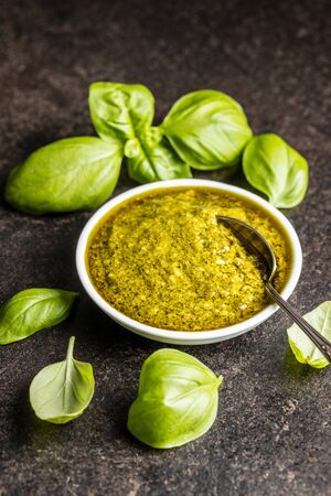 Green basil pesto dip sauce in bowl and basil leaves on black table.の写真素材