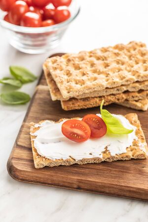 Dieting knackebrot. Crispbread with creamy cheese, cherry tomato and basil leaf on kitchen table.の写真素材