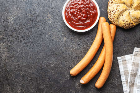 Fresh frankfurter sausages with bun and ketchup on black table. Top view.の写真素材