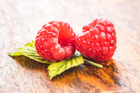 Ripe red raspberries and green leaves on wooden table.