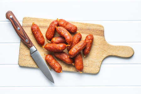 Mini salami sausages on wooden cutting board on white table. Top view.の写真素材