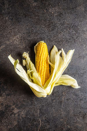 Uncooked corn cob on black table. Top view.