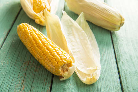 Uncooked corn cob on green wooden table.