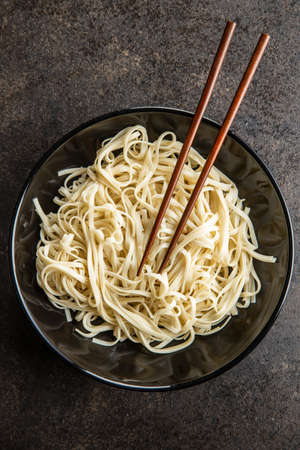 Cooked udon noodles. Traditional Japanese noodles in plate on black table. Top view.の写真素材