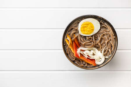 Asian noodle soup with soba noodles, vegetable and egg in bowl on white table. Top view.の写真素材
