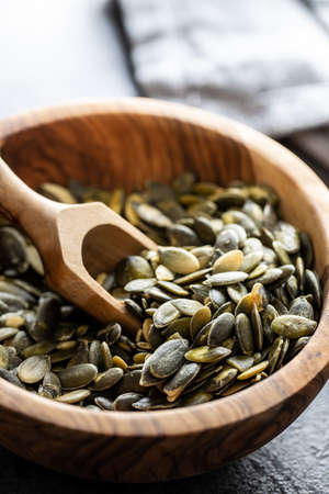Peeled pumpkin seeds in wooden bowl and scoop on black table.の写真素材