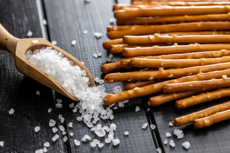 Salty sticks. Crunchy pretzels and coarse salt in wooden scoop.の写真素材