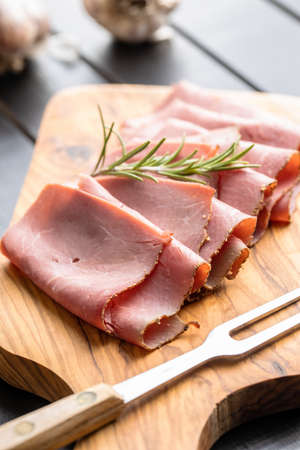 Sliced beef ham on cutting board on black table.