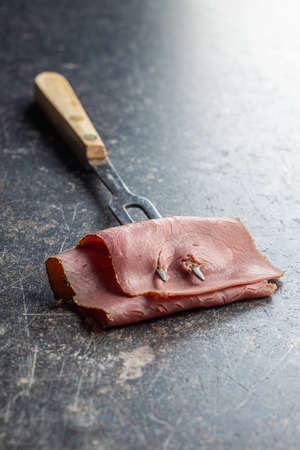 Sliced beef ham and fork on black table.の写真素材