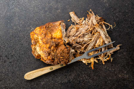 Pulled pork meat with fork on black table. Top view.